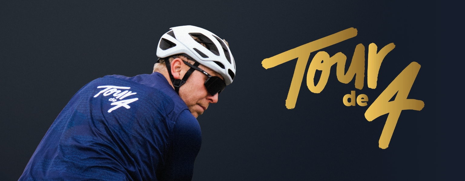 Chris Hoy fährt auf einem Fahrrad und trägt ein Tour de 4-Trikot mit dem Schriftzug "Tour de 4" neben sich auf blauem Hintergrund